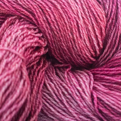 A close-up of variegated pink and purple yarn, showing the texture of the twisted wool fibers.