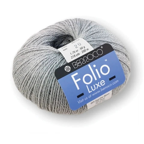 A skein of light gray yarn with a blue and black Berroco Folio Luxe label, shown on a clean white background.