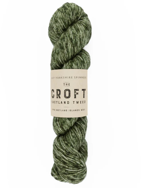 A skein of green and beige marled yarn with a paper label reading 'The Croft Shetland Tweed' on a white background.