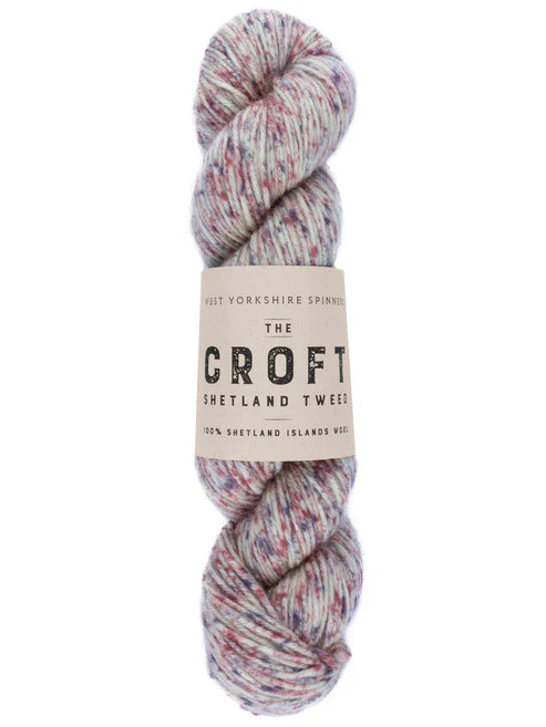 A skein of yarn with a cream paper label reading 'The Croft Shetland Tweed' on a plain white background. The yarn is variegated with flecks of pink, blue, and gray on a light base.