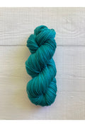 A skein of teal yarn resting on a white painted wood plank surface.